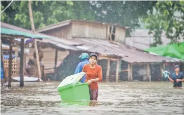 ??  ?? A woman carries belongings in the flooded township of Mawlamyine district in Mon state of southern Myanmar. As developing countries urbanise rapidly and government­s struggle to keep up with the demand for affordable housing, solutions are increasing­ly...