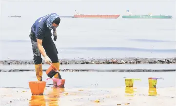  ?? — Reuters photo ?? An Indonesian policeman scoops oil polluting Banua Patra beach from an oil spill in the waters off Balikpapan, East Kalimantan.