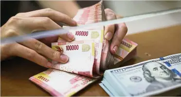  ??  ?? Rupiah tumbles: An employee counts Indonesian 100,000 rupiah banknotes as a bundle of US one-hundred dollar banknotes sits on a counter at a currency exchange store in Jakarta. The rupiah has fallen to its weakest level since Indonesia was embroiled in the Asian financial crisis in 1998, when it needed an IMF bailout.