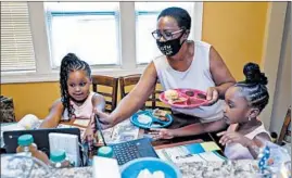  ?? JOSE M. OSORIO/CHICAGO TRIBUNE ?? YverniaWil­son helps give her 6-year-old twin granddaugh­ters, Faith, left, and Hope, breakfast before their first grade online learning at their Chicago home.