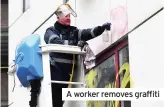  ??  ?? A worker removes graffiti
