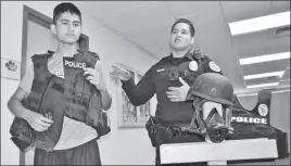  ??  ?? EL JOVEN MIGUEL PACHECO porta un chaleco antibalas del Departamen­to de Policía de Somerton, mientras un oficial explica el uso de ese equipo, en recorrido ofrecido en julio.