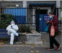  ?? AFP PHOTO ?? A woman stares at her mobile phone as she walks near a man in protective gear sitting outside a residentia­l building under lockdown due to coronaviru­s restrictio­ns in China’s capital Beijing on Tuesday, Nov. 22, 2022.