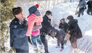  ?? PAUL CHIASSON / THE CANADIAN PRESS ?? A family originally from Somalia is helped into Canada by RCMP officers along the border near Hemmingfor­d, Que., on Friday. A number of refugee claimants have been braving the elements to illicitly enter Canada from the U.S.