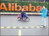  ?? (AP) ?? In this file photo, a man talks on his phone as a woman rides on an electric bike past a company logo at the Alibaba Group headquarte­rs in Hangzhou in eastern China’s Zhejiang province.