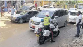  ?? (Photos: Philp Lemonte) ?? A policeman looks on helplessly as traffic piles up in this section of Anchovy yesterday, resulting from heavy overnight rain in the area on Friday.