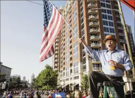  ?? CHAD RHYM / CHAD.RHYM@AJC.COM ?? In the middle of the AJC Peachtree Road Race course, Henry Schwab sits atop a ladder, swinging an American flag to cheer on the participan­ts.