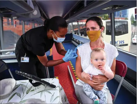  ??  ?? Hazel Hiram of the Scottish Ambulance Service, gives Gillian Fergusson, 40, an injection of a Covid-19 vaccine as Fergusson holds her 10-month-old