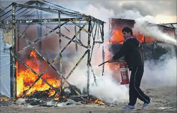  ?? CARL COURT / GETTY ?? Un inmigrante tratando de apagar ayer el fuego que devora una de las chabolas de la jungla de Calais