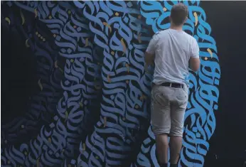  ?? Raid Madhaa ?? Calligraph­y artist Raid Madhaa working on a mural in an underpass at Baghdad’s Tahrir Square, above, and with fellow protesters at another of his murals at the square, right