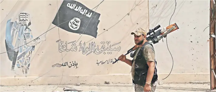  ??  ?? Un miembro de las fuerzas de seguridad iraquí camina frente a un grafitti con la bandera del Estado Islámico, en Shirqat.
