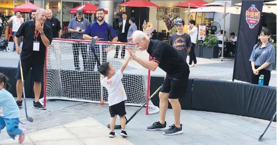  ??  ?? Flames legend Lanny McDonald high-fives a young Chinese fan during fanfest activities in Shenzhen, China on Thursday. The team arrived Wednesday. Please see C2 for story.