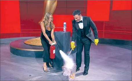  ?? Photograph­s from ABC ?? JENNIFER ANISTON helps host Jimmy Kimmel extinguish a fire during a comedy bit Sunday night at the largely empty Emmy Awards.