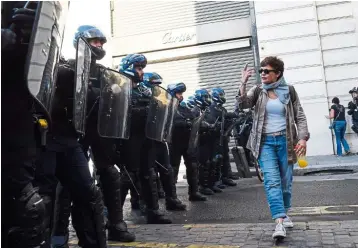  ?? — AFP ?? Making a point: Awoman gesturing as she walks past gendarmes blocking a street before a demonstrat­ion called by the ‘yellow vest’ movement in Paris.