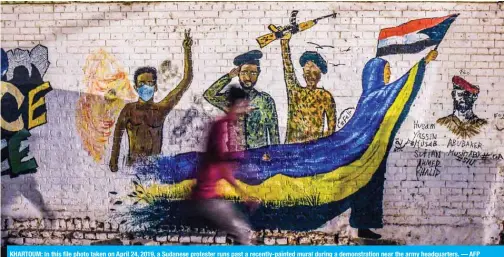  ??  ?? KHARTOUM: In this file photo taken on April 24, 2019, a Sudanese protester runs past a recently-painted mural during a demonstrat­ion near the army headquarte­rs. — AFP