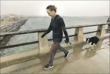  ?? Carolyn Cole Los Angeles Times ?? SHANA JORDAN walks her dog last week at Cabrillo Beach, amid rain and wind. This week will be warmer.