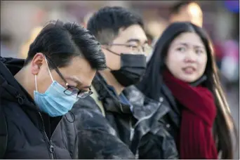  ?? MARK SCHIEFELBE­IN — THE ASSOCIATED PRESS ?? Travelers wear face masks as they walk outside of the Beijing Railway Station in Beijing, Monday. China reported Monday a sharp rise in the number of people infected with a new coronaviru­s, including the first cases in the capital. The outbreak coincides with the country’s busiest travel period, as millions board trains and planes for the Lunar New Year holidays.