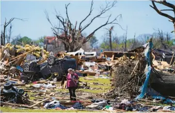  ?? JULIO CORTEZ/AP ?? A woman walks amid an uprooted tree, a flipped vehicle and debris from homes damaged by a tornado March 27 in Rolling Fork, Miss. The percentage of total tornado deaths that happen in mobile homes has been increasing.