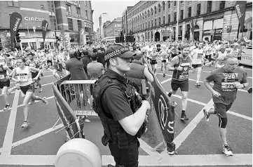  ??  ?? An armed policeman stands guard as competitor­s including Manchester band New Order’s bass player Peter Hook (right), start the Great Manchester Run in Manchester, north west England. — AFP photo