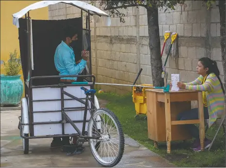  ??  ?? Gerardo Ixcoy teaches fractions to 14-year-old Brenda Morales from his secondhand adult tricycle he converted into a mobile classroom in Santa Cruz del Quiche, Guatemala. The 27-year-old teacher uses a sponge mop to serve as a safe distance reminder between him and his students amid the new coronaviru­s pandemic. (AP/Moises Castillo)