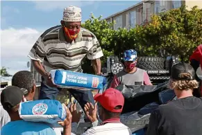  ??  ?? Danny, a senior member of the Hard Livings gang, distributi­ng food with rival gang members in Manenberg.