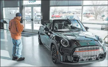  ?? David Zalubowski The Associated Press ?? A man looks at a 2024 Cooper S convertibl­e at a Mini dealership in Loveland, Colo. Auto prices are starting to drop, helping to slow overall consumer price increases.