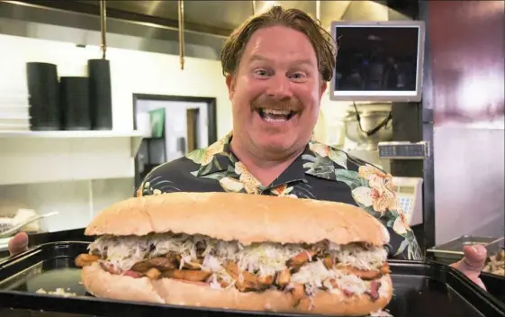  ??  ?? “Man vs. Food” host Casey Webb holds the Stuffaluff­agus, a sandwich made with an entire loaf of bread, at Steel City Samiches in Indiana, Pa.