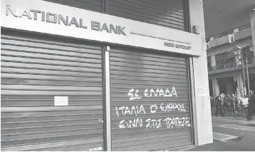  ??  ?? Demonstrat­ors pass by a shut down National Bank of Greece branch. Greece does not need more austerity at this time, and in fact spending cuts have gone too far already, two senior Internatio­nal Monetary Fund officials said. — AFP photo