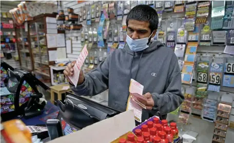  ?? MATT STONE PHOTOS / HERALD STAFF ?? WINNING WAYS? Sunny Patel, co-owner of Joe’s Market Place, runs the lottery machine Monday in his store in Quincy. A sign in the window shows that both Powerball and Mega Millions have jackpots over $500 million.