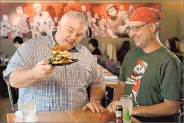  ?? Discover y Channel ?? CHEF TODD FISHER marvels at Des Moines’ Zombie Burger owner George Formaro with his Walking Ched burger, which also includes plenty of bacon, breaded and deep-fried macaroni, cheese and onion.