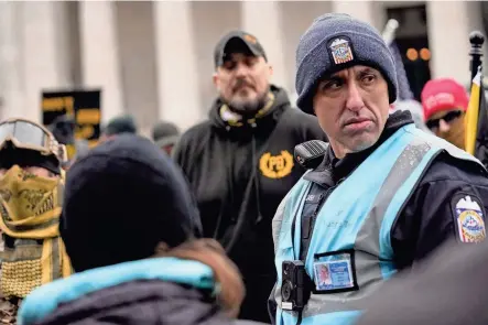  ?? BROOKE LAVALLEY/COLUMBUS DISPATCH ?? Officer Joshua Rhoads, a member of the Columbus police dialogue team, keeps distance between a group of far-right Proud Boys extremist group members and groups of counter-protesters who had gathered outside the Ohio Statehouse on the anniversar­y of the January 6 insurrecti­on.