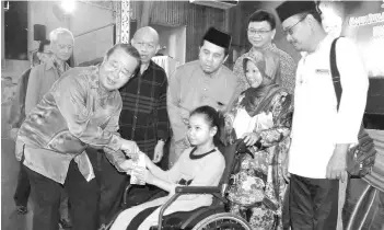  ??  ?? Radin (left) presenting Raya money to a disabled child accompanie­d by her mother. Also seen is Jamawi (third right).