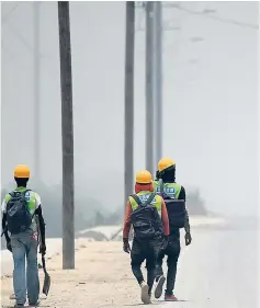  ?? RICARDO MAKYN ?? Workmen walk through smoke on a section of the Mandela Highway yesterday.