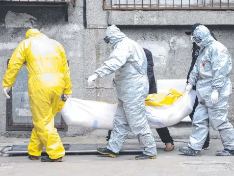  ?? Picture: AP ?? CRISIS: Funeral home workers in hazmat suits remove the body of a suspected coronaviru­s victim from a building in Wuhan.