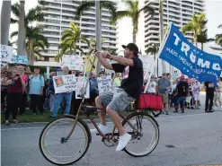  ?? —AP ?? FLORIDA: Dylan Moye rides his bike past Donald Trump protesters gathered in downtown West Palm Beach, Florida.