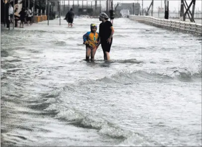  ?? Vincent Yu ?? People walk through floodwater­s caused by Typhoon Mangkhut on the waterfront Sunday in Hong Kong. The Associated Press