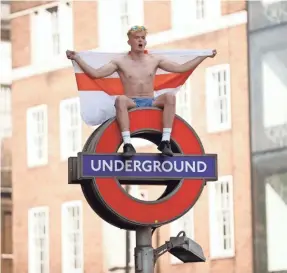  ?? MATT DUNHAM/AP ?? A fan sits with a St George’s Cross England flag atop of a London Undergroun­d sign.