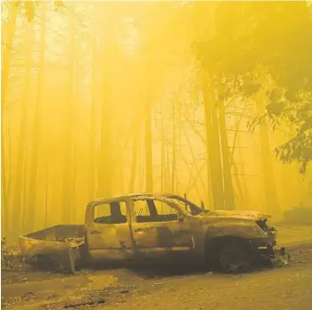  ?? MARCIO JOSE SANCHEZ/AP ?? A burned-out vehicle is left in front of a fire-ravaged residence as smoke from the CZU August Lightning Complex Fire fills the sky Saturday in Boulder Creek, California. Crews continued to fight the blaze on Sunday.