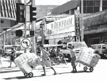  ?? MACKY LIM ?? MORNING GRIND. Store helpers endure the morning heat as they cart in stocks to their store along Ramon Magsaysay Avenue in Davao City yesterday.