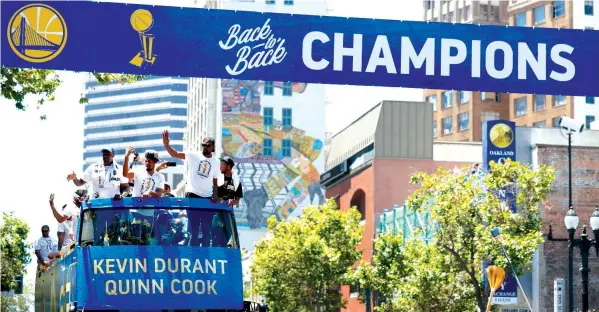  ?? ASSOCIATED PRESS ?? A champions banner is placed overhead as a bus carrying Golden State Warriors' Kevin Durant and Quinn Cook rides down the route during the team's NBA basketball championsh­ip parade in Oakland, Calif.