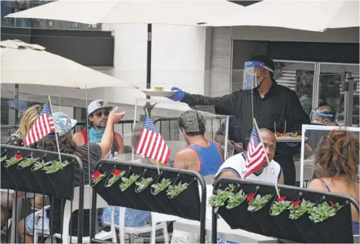  ?? ROBYN BECK/AFP VIA GETTY IMAGES ?? A waiter serves food Saturday in Manhattan Beach, California, one of several big states facing a virus resurgence.