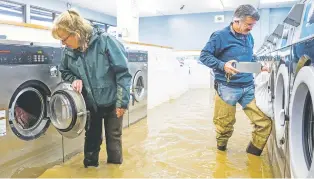  ?? NOAH BERGER/THE ASSOCIATED PRESS ?? Pamela and Patrick Cerruti empty coins from Pajaro Coin Laundry as floodwater­s surround machines Tuesday in Pajaro in Monterey County, Calif. ‘We lost it all. That’s half a million dollars of equipment,’ said Pamela Cerruti, who added they plan to rebuild.