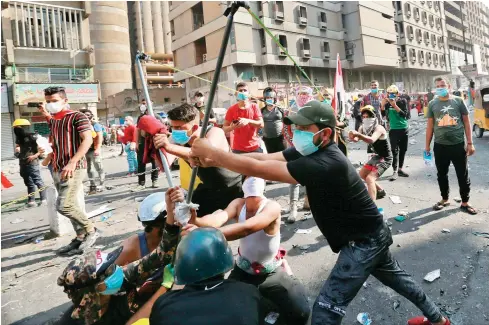  ??  ?? Protesters use a slingshot to throw a stone at police in downtown Baghdad. Security forces fired live rounds and tear gas at protesters on Friday, killing three people, in bloody confrontat­ions that continued despite influentia­l Shiite leader Ali Al-Sistani’s call for calm.