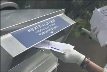  ?? SETH WENIG ?? FILE - In this July 7, 2020, file photo a woman wearing gloves drops off a mail-in ballot at a drop box in Hackensack, N.J. The November election is coming with a big price tag as America faces the coronaviru­s pandemic. The demand for mail-in ballots is surging, election workers are in need of training and polling booths might have to be outfitted with protective shields.