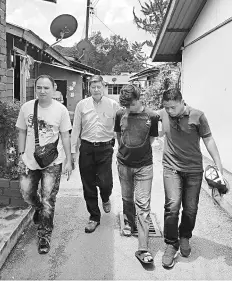  ??  ?? The suspect (second right) being led away by police following his arrest at a house in Kampung Tabuan.