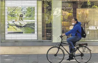  ?? JULIO MUÑOZ ?? Un hombre en bicicleta pasa por delante de un comercio cerrado en Sevilla.