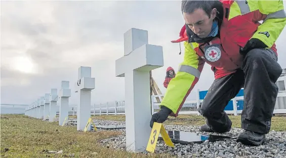  ??  ?? El trabajo en el cementerio de Darwin. Un tecnico de la Cruz Roja en plena tarea. La difusión de unas fotos provocó indignació­n.