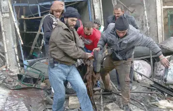  ?? — AFP ?? Syrian men evacuate a victim from a building following an air strike on the village of Maaret al Numan, in the province of Idlib, on Sunday.