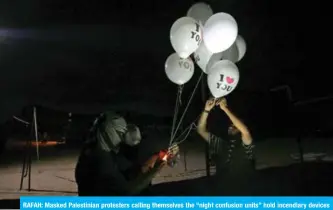  ??  ?? RAFAH: Masked Palestinia­n protesters calling themselves the “night confusion units” hold incendiary devices attached to balloons to be flown towards Israel near the Gaza-Israel border in the southern Gaza Strip on Sept 26, 2018. — AFP