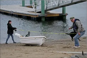  ?? STUART CAHILL — BOSTON HERALD ?? Paul Noggin pulls his boat out of the water at the while Residents take in air along the Hingham Bathing Beach Thursday.